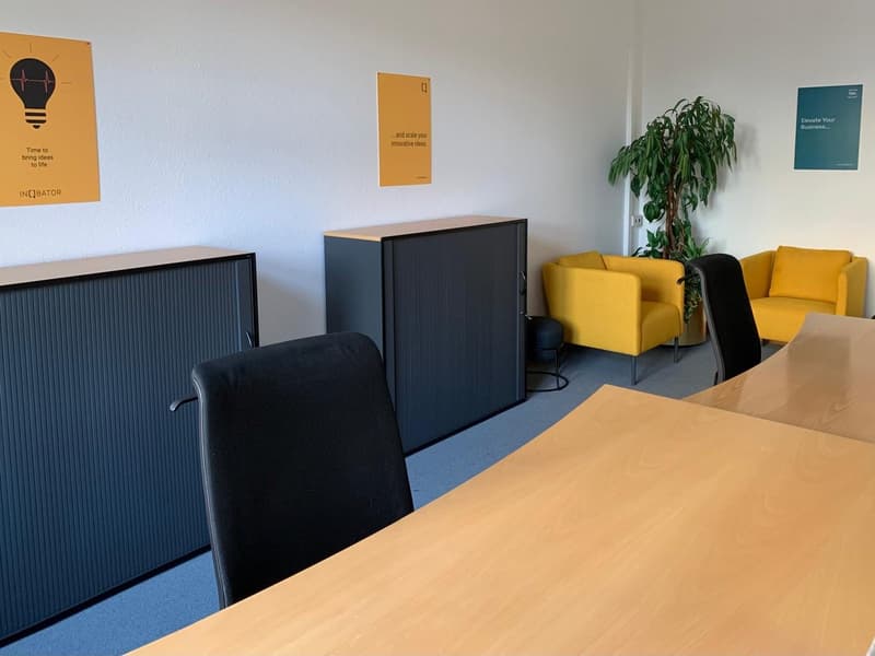 Meeting room with black and yellow chairs, desks, cabinets, plant, and motivational posters on the wall.