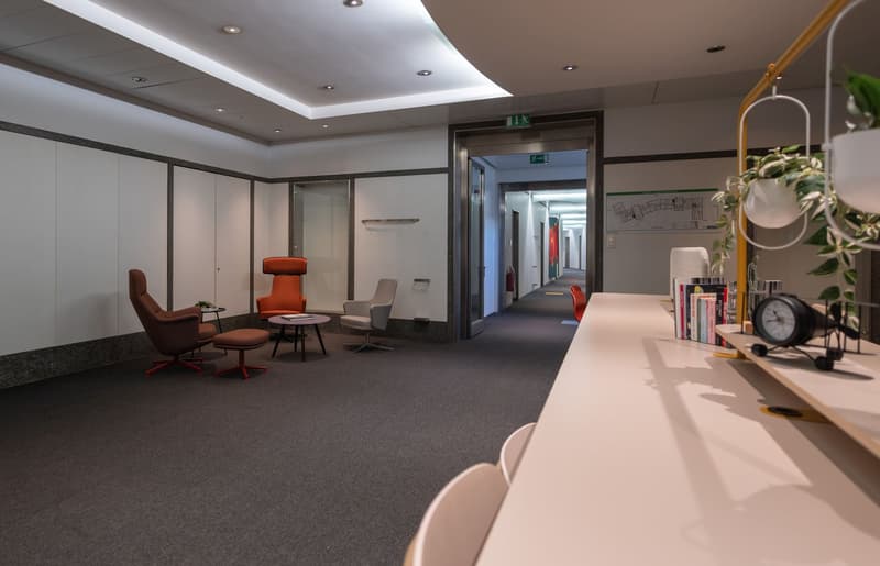 empty waiting room with modern chairs, tables, and lighting, cabinets on the left wall, books and a clock on the desk