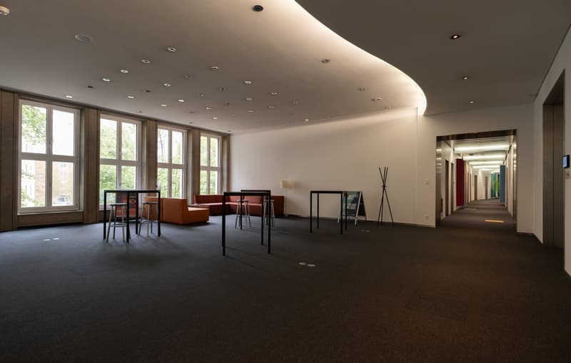 an empty rectangular hall, 4 large windows, carpeted floor, tables, chairs