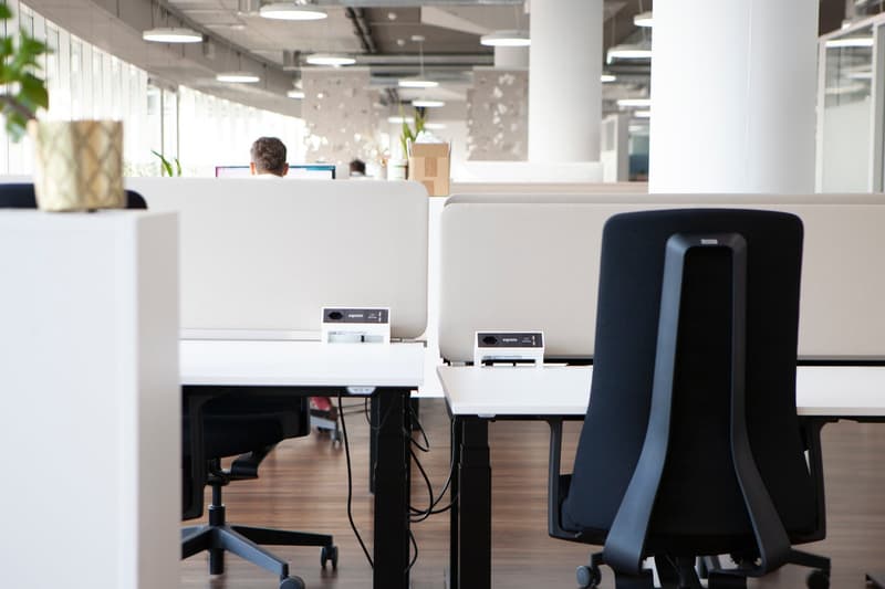 Two desks, two black chairs, modern chairs, wooden floors, lights on ceiling, box on floor