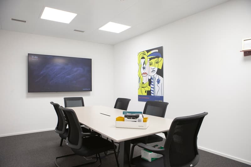 Conference room with a long table, black chairs, digital frame, painting on the wall, and a monitor on the wall.