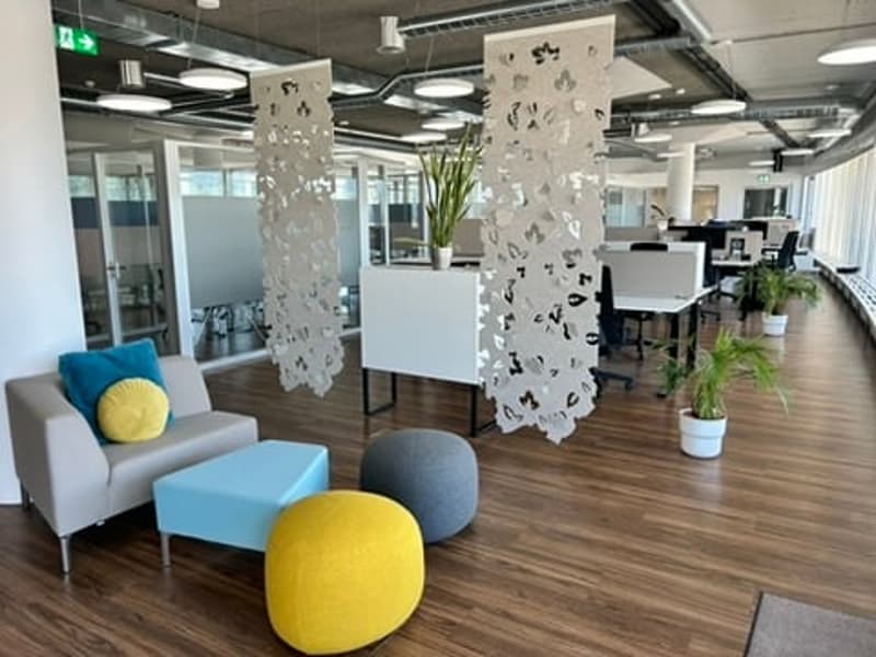 modern open office space with hardwood floors, office furniture, white partitions, office plants, round pillows on couch, and colorful round ottomans
