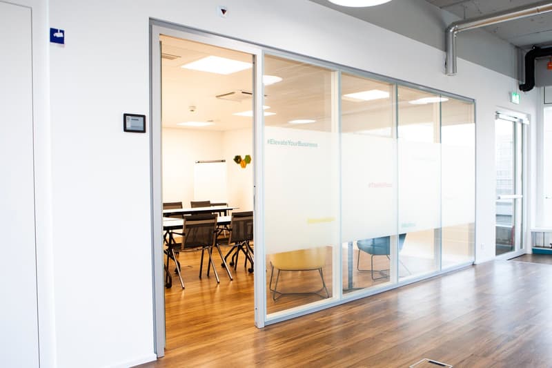 modern office room, glass walls, wood flooring, tables and chairs, whiteboard, natural light
