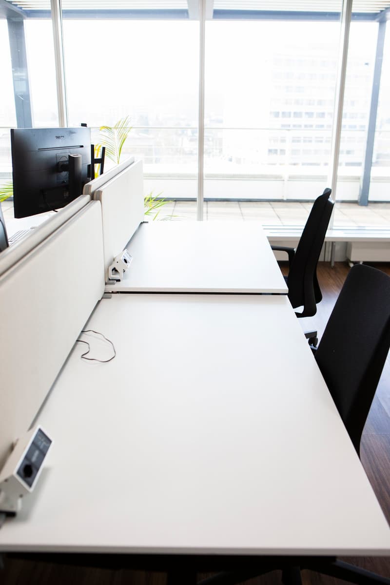 modern office setup, white desks, glass walls, computer screens, black office chairs, plants
