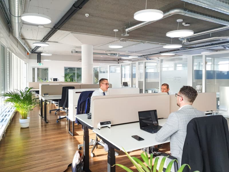 Spacious office with glass partitions, desk, laptop, cell phone, jacket on chair, plant.