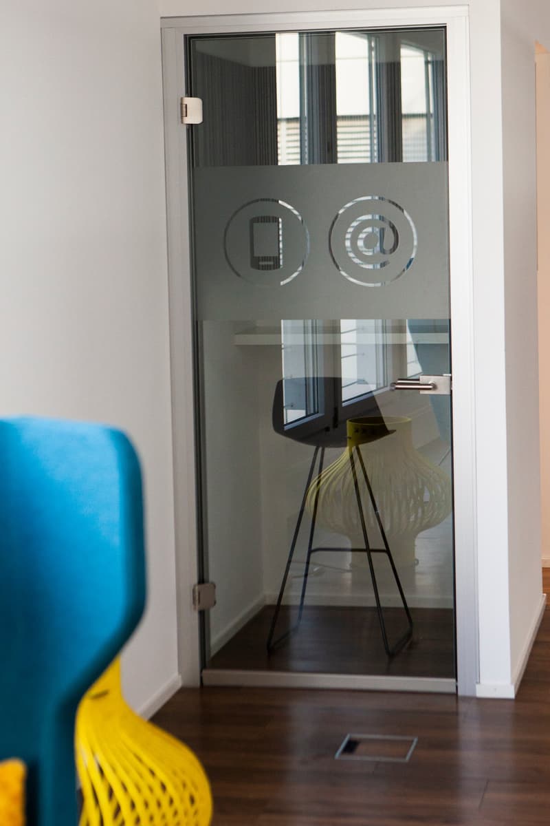 An open room with wooden floor, white walls, and a glass door with icons.