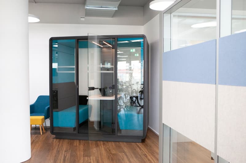 office with a meeting booth, glass partition, blue seats, glass wall, wooden floor