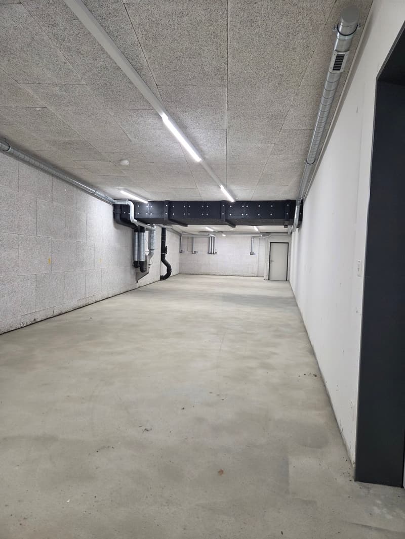 Empty parking area with concrete floor, white walls, and ceiling with lights and pipes.