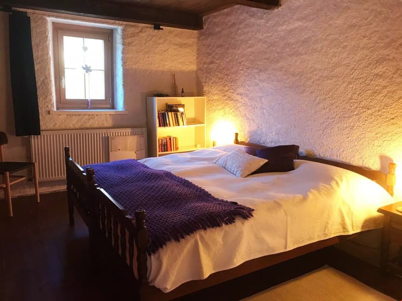Bedroom with a wooden bed, bookshelf, white walls, window, radiator, and chair.