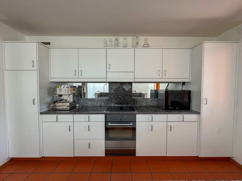 modern kitchen with white cabinets, black granite countertop, stainless steel oven and stove, white tiled floor, large glass wall mirror, microwave, coffee maker