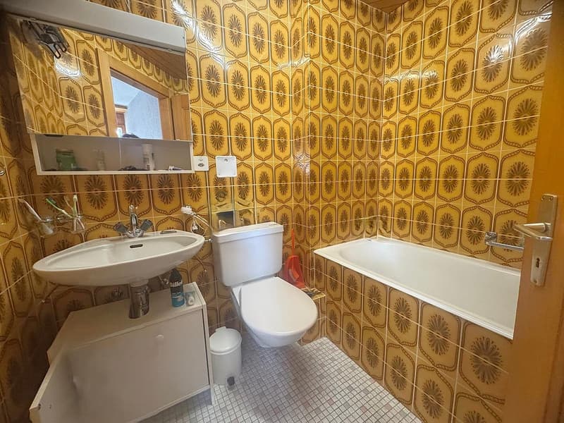 Bathroom with white sink, white toilet, white bathtub, yellow tiles, small cabinet, trash can, and a mirror.