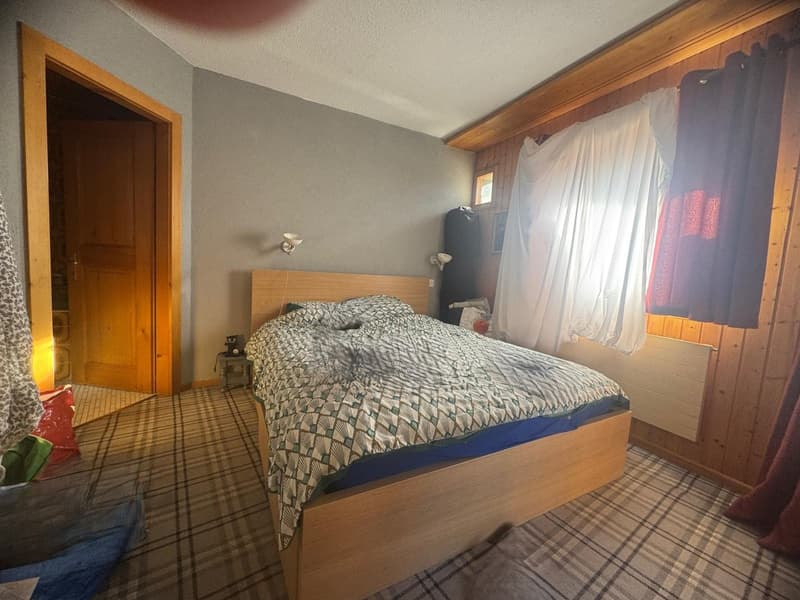 bedroom with wooden bed, wooden wall, plaid floor, lamp, window with white curtain