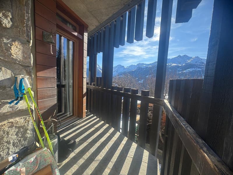 balcony with wooden railings, stone wall, ski poles, ski boots, view of mountains