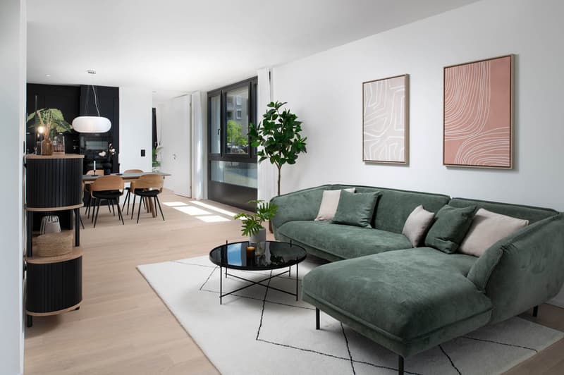 Green L-shaped sofa, glass coffee table, rug, potted plants, dining area with table and chairs, modern light fixture