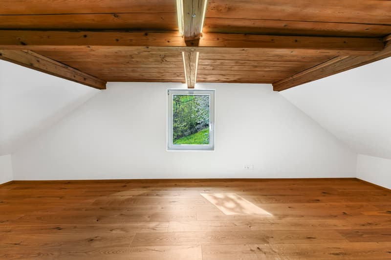 empty attic room with wooden floor and ceiling, white walls, small window