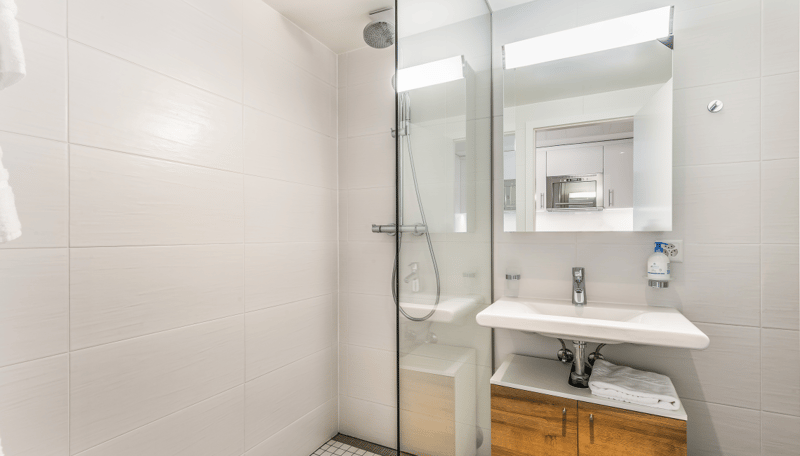 Modern bathroom with white tiles, glass shower enclosure, vanity with sink, and a built-in dishwasher