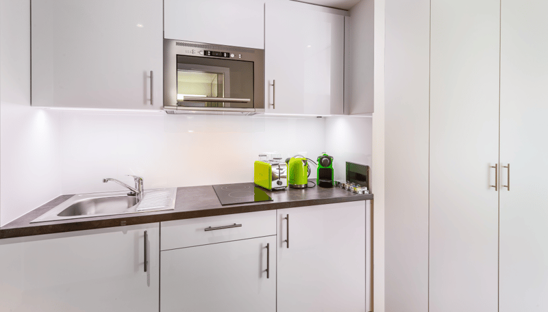 Modern kitchen with white cabinets, stainless steel sink, built-in microwave, and small kitchen appliances like a coffee maker and blender on the countertop.