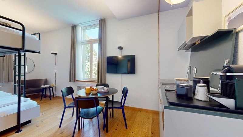 small room with wooden floor, round dining table, 4 chairs, bunk bed, sofa, TV, mirror, countertop, coffee machine, sink