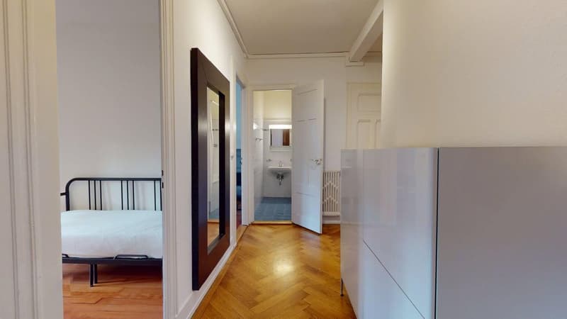 Empty room with hardwood floors, single bed, a large mirror, and an open bathroom door.