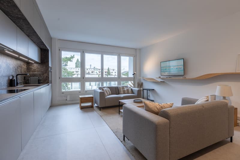 modern living room, open to the kitchen, large windows, sofas, coffee table, TV mounted on the wall, wooden floor, white walls