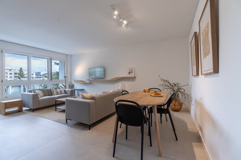 modern living room with large windows, beige carpet, sofas, dining table, dining chairs, coffee table, artwork, TV stand, wall lamp, potted plant