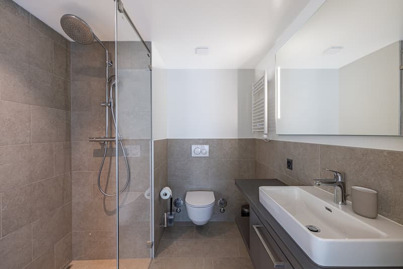 modern bathroom with shower, toilet, sink, mirror, and tiled walls