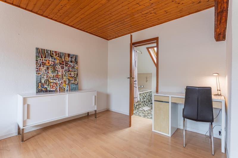 room with wooden floor, white walls, wooden ceiling, desk, lamp, cabinet with drawers, and an abstract painting on the wall