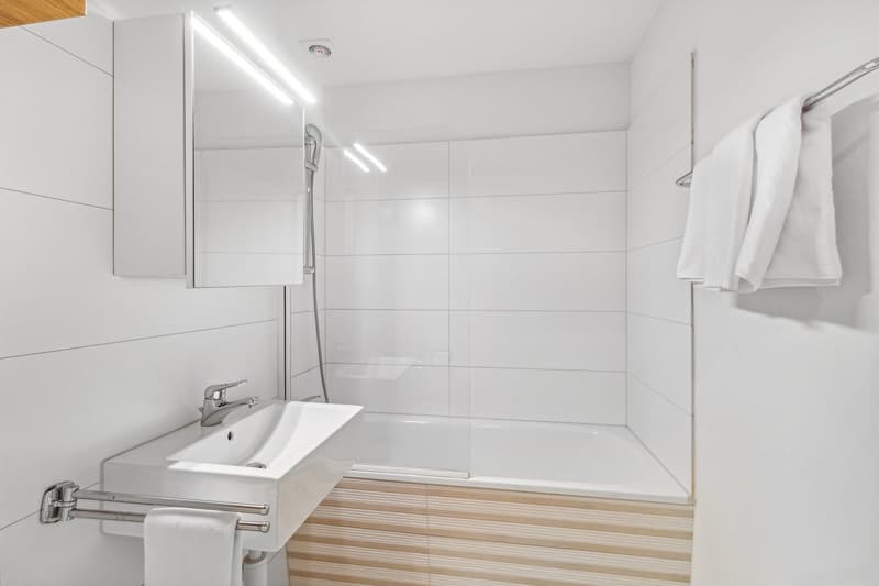 modern bathroom, white tiles, white sink, glass shower enclosure, towels, shower head