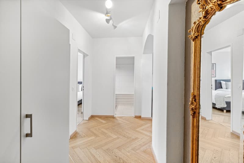 Wide hallway, parquet floor, mirror, open doors to other rooms, ceiling lights