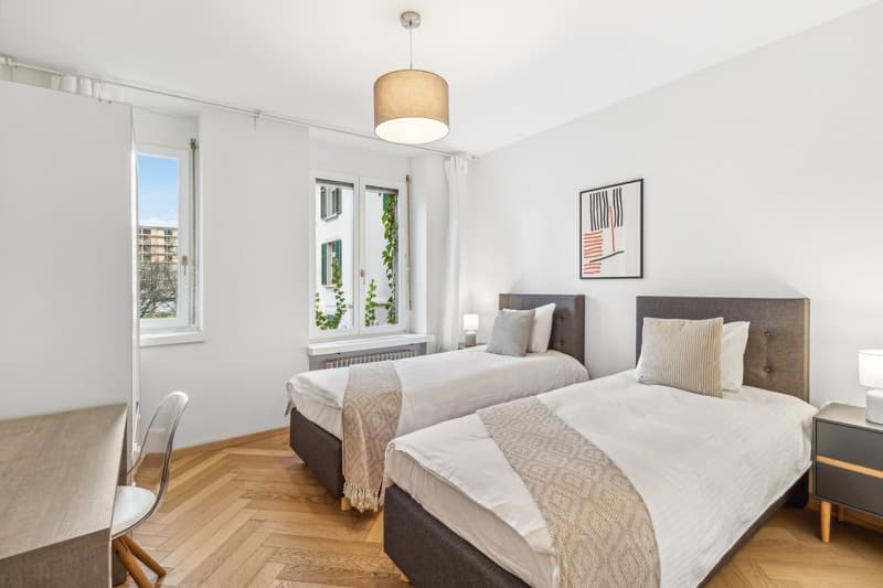 Two beds, white walls, wood floor, nightstands, lamps, white curtains, picture frame