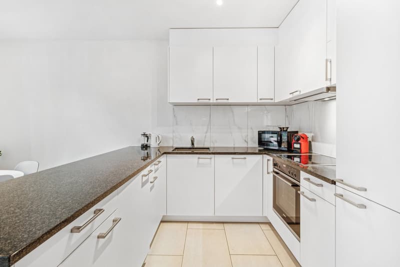 modern kitchen with white cabinets, marble countertop, tiled floor, appliances like microwave, coffee maker, kettle, stove, oven, dishwasher