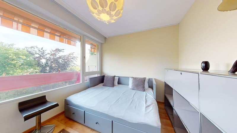 Bedroom with gray storage drawers, white bed, bedside table, stool, large window, balcony, wooden floor