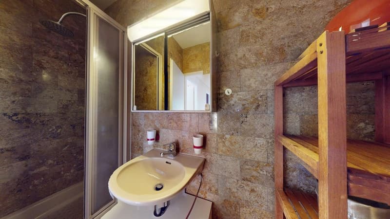 Bathroom with a tiled wall, shower, a sink, a mirror, and a wooden shelf.