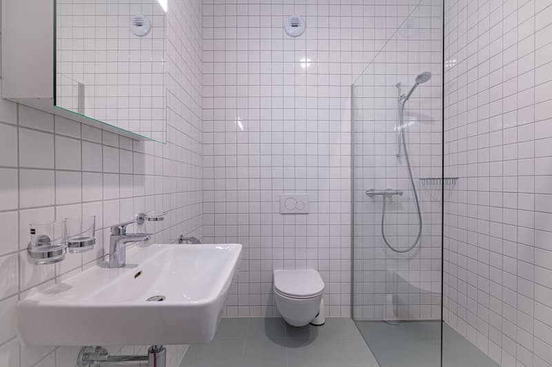 modern bathroom with white tiles, white sink, white toilet, glass shower enclosure, shower head, and faucet