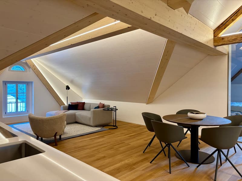 A sofa, a carpet, a wooden desk, chairs, a round table, lamps, sink, window