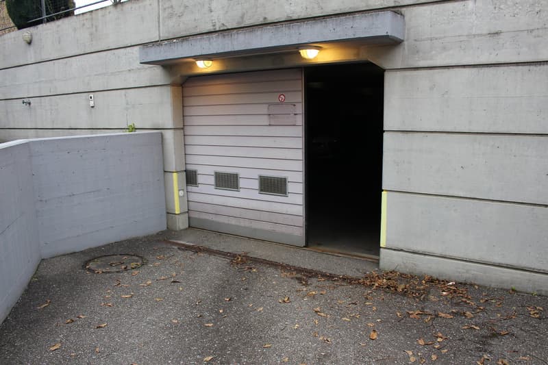 garage entrance with automatic door, covered parking space, grey concrete wall, two light fixtures above door