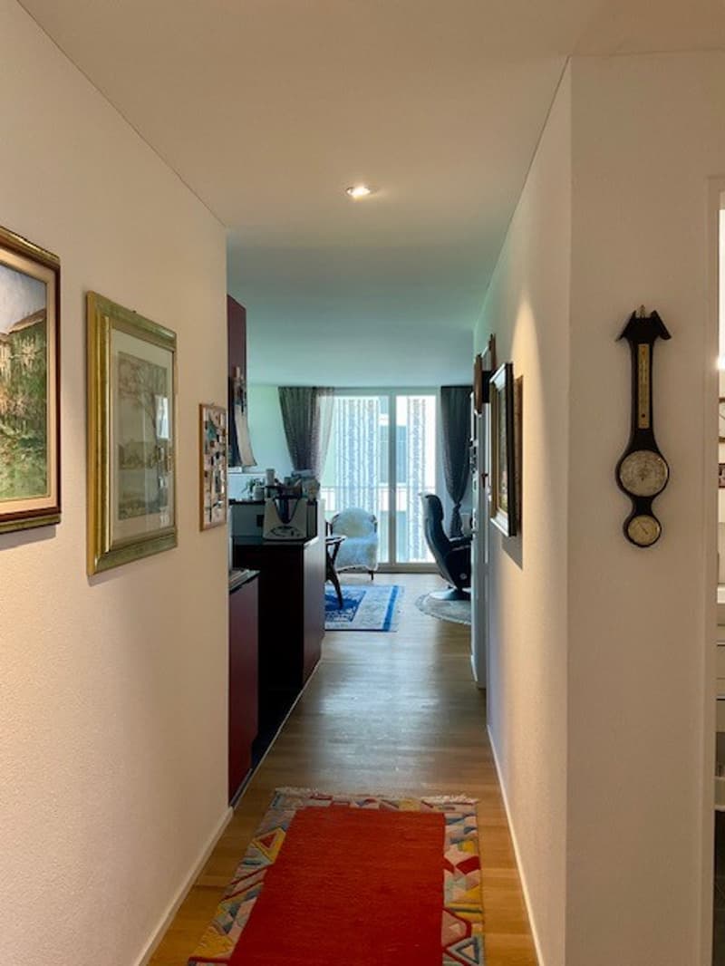 White walls, wood floor, hallway, red carpet, framed pictures, small rug in the living room, dining table and chairs, chair, small rug, bed, clock on the wall