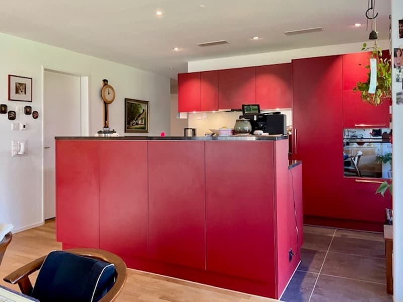 modern kitchen with red cabinets, wooden countertop, red floors, microwave, coffee maker, wall clock, picture frames, open door, wooden chair, potted plants