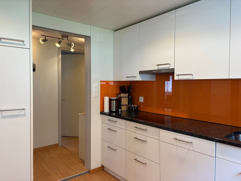 modern kitchen with white cabinets, orange backsplash, black countertops, stainless steel sink, black stove, white ceiling, wooden floor