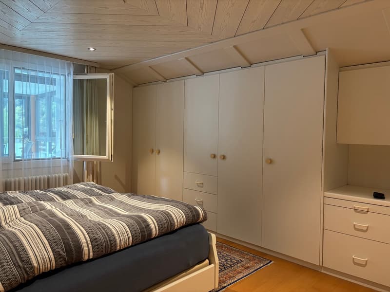 Bedroom with bed, large wardrobe, window with curtains, wooden floor, rug, radiator