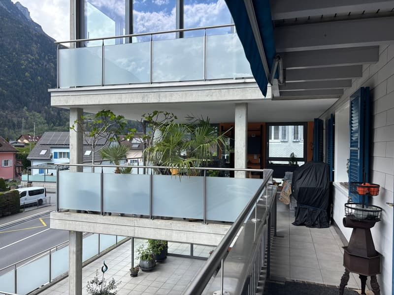 Two-story building with a balcony, glass railings, tiled floor, and a view of the mountains.