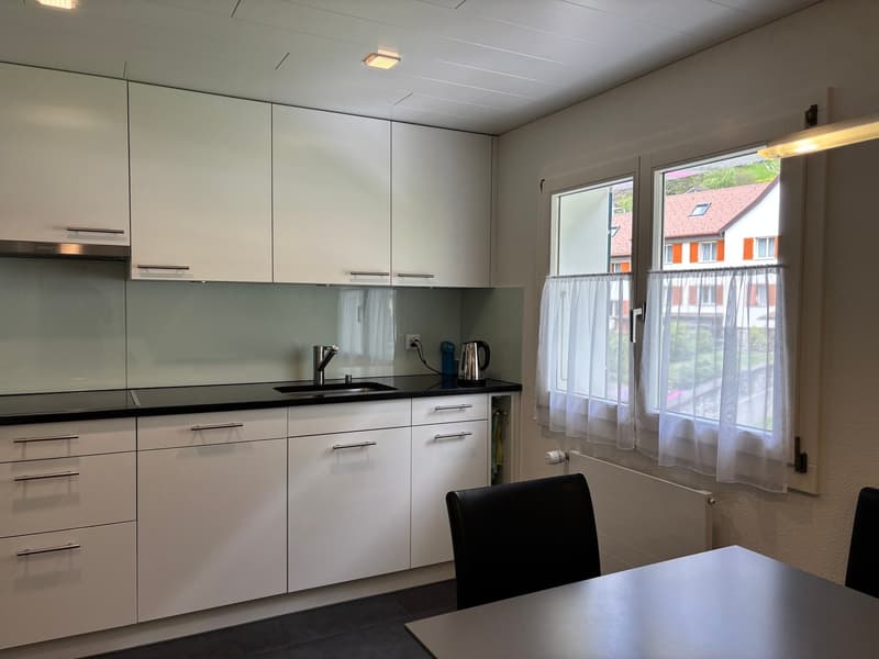 modern kitchen with white cabinets, black countertops, stainless steel sink, faucet, white chairs, white curtains, white radiator, kettle, power outlet, window with view