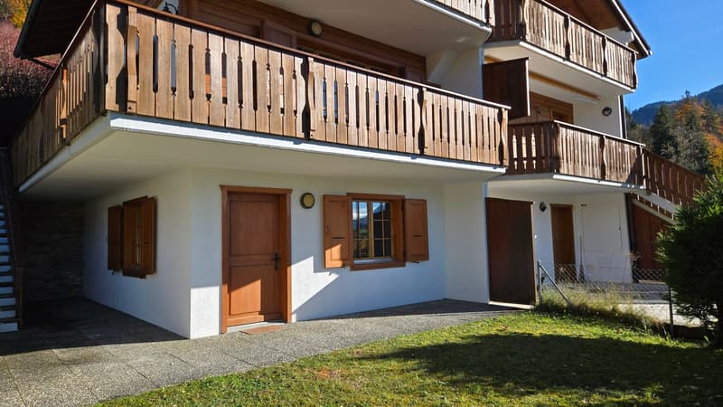 Two-story house, white painted exterior, wooden balcony with railings, wooden shutters, large windows, raised ground floor, driveway