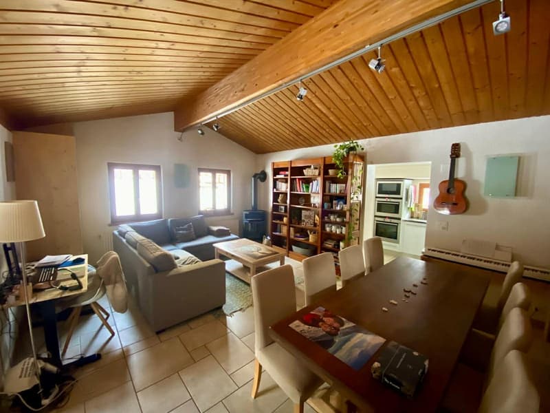 Living room with couch, table, bookshelves, mounted guitars, and a piano. White walls, wooden ceiling, lamps, and tiled flooring.