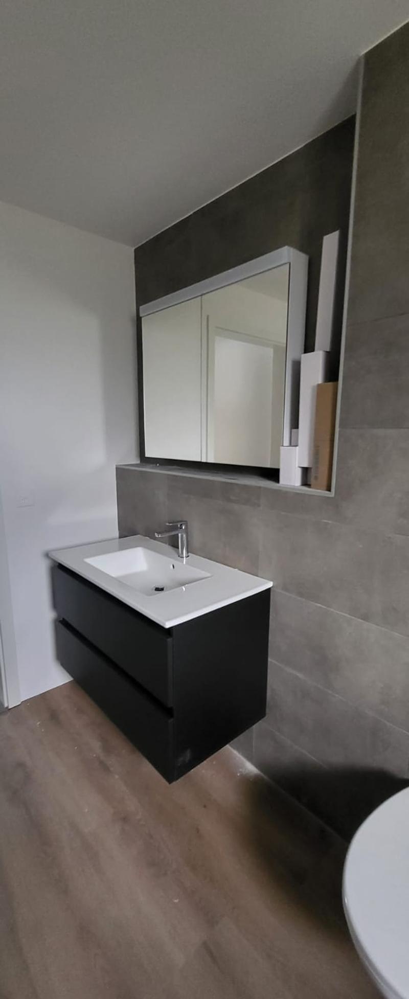 Bathroom with a white sink, black cabinet, mirror, and gray tiles