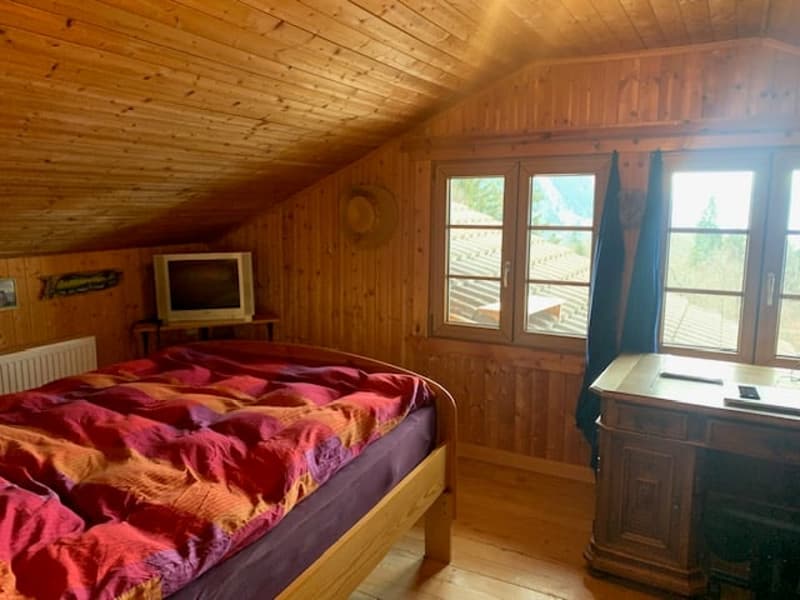 Cozy wooden bedroom with a large bed, wooden walls and ceiling, and windows overlooking a balcony or terrace.