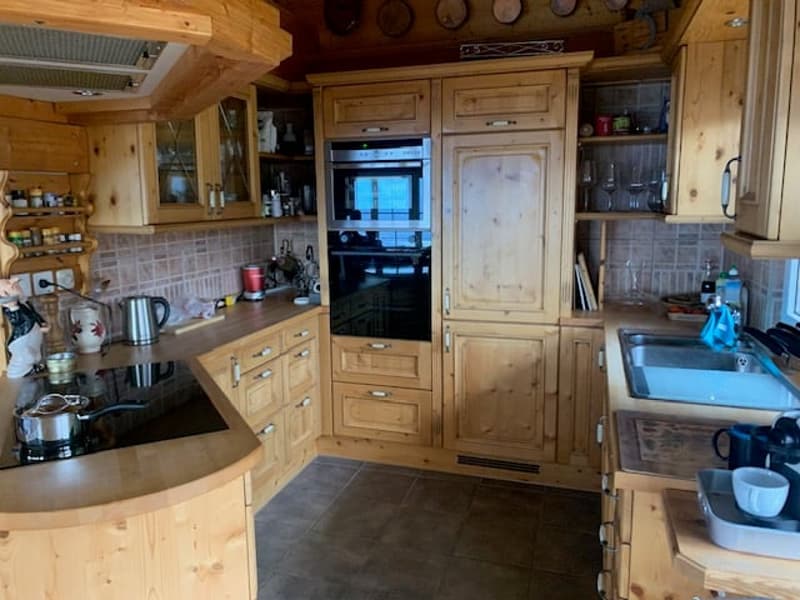 Rustic wooden kitchen with built-in cabinets, drawers, and appliances. The kitchen has a tile backsplash and a sink with a faucet. There are various kitchen utensils and cookware visible on the countertops and shelves.