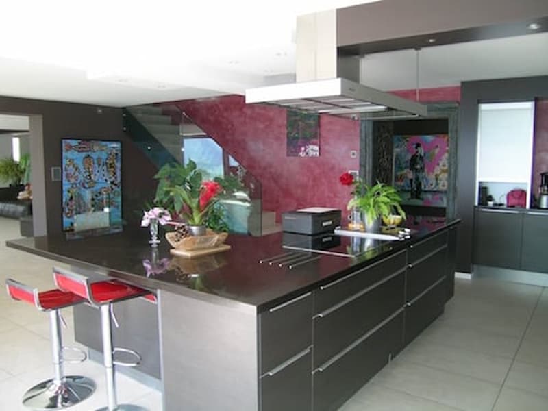 modern kitchen with island, red walls, white ceiling, red stools, plants, gas stove, sink, cabinets, artwork