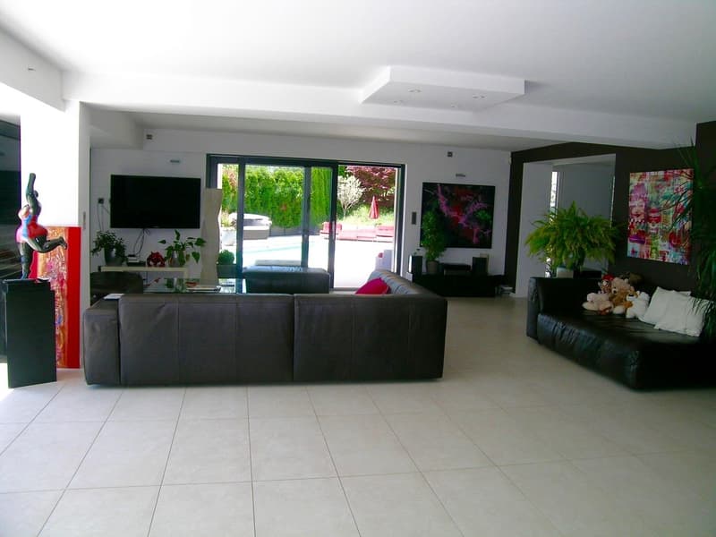 large living room, two sofas, TV, glass doors, pool view, plants, paintings