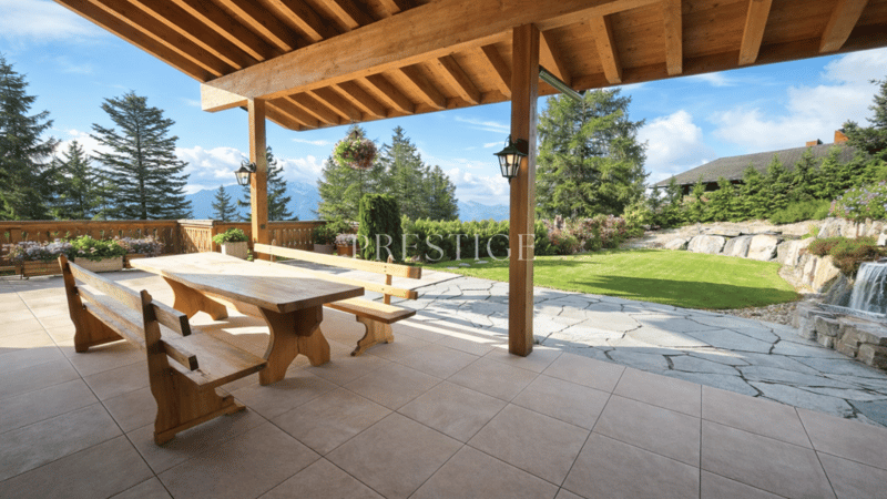 Balcony with wooden tables and benches, covered by wooden ceiling, with view over garden and mountains